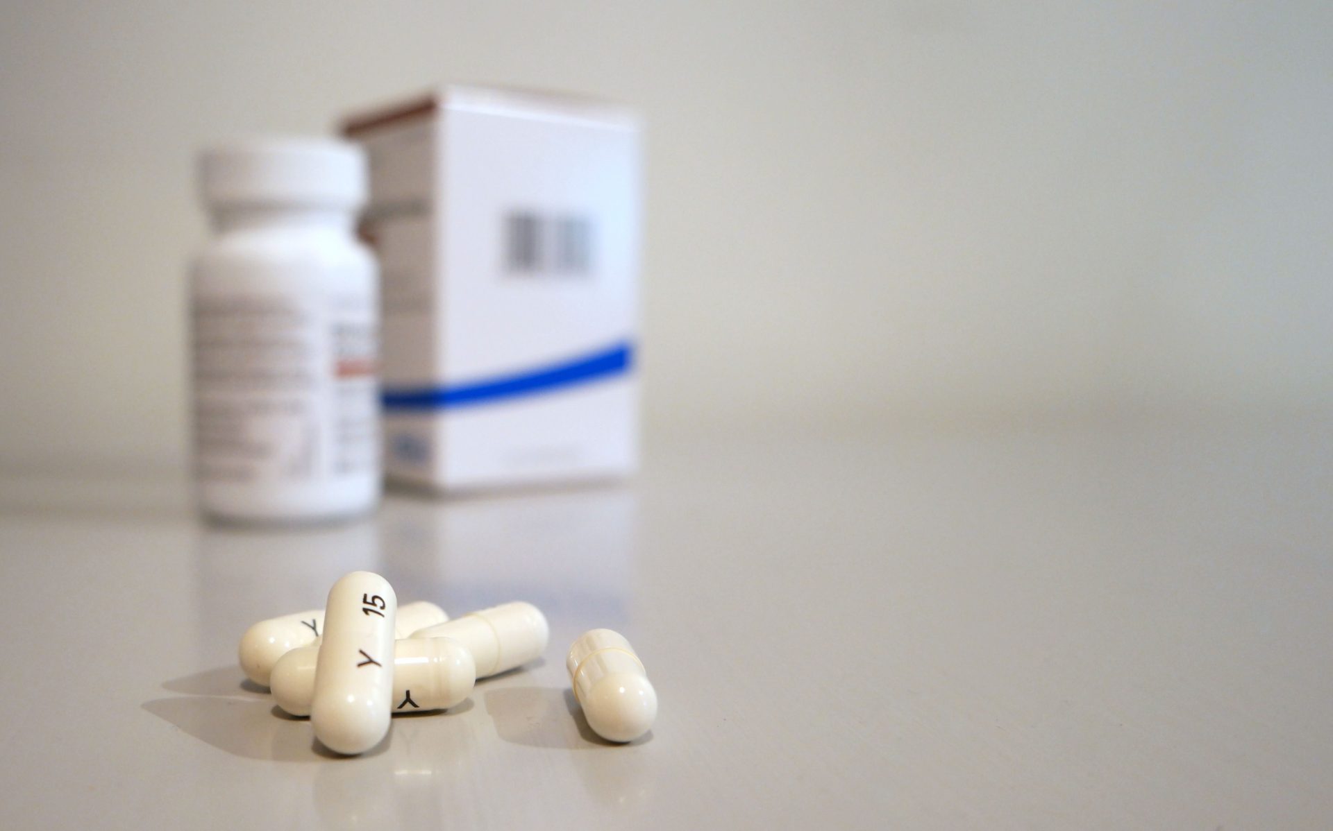 Gros plan de capsules blanches avec un flacon et une boîte de médicament en arrière-plan.