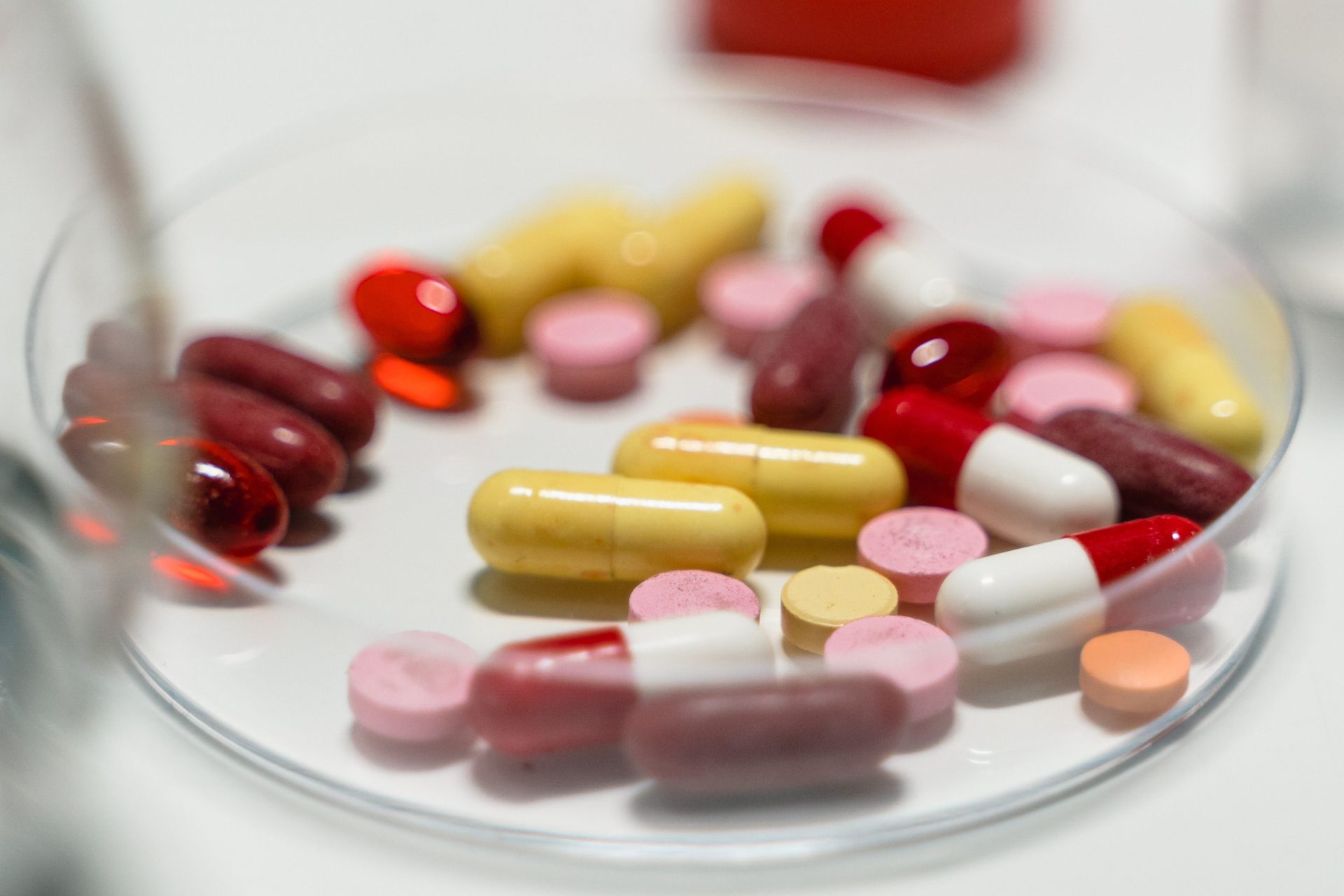 Assortiment de pilules et de capsules colorées disposées sur une boîte de Petri pour analyse pharmaceutique.