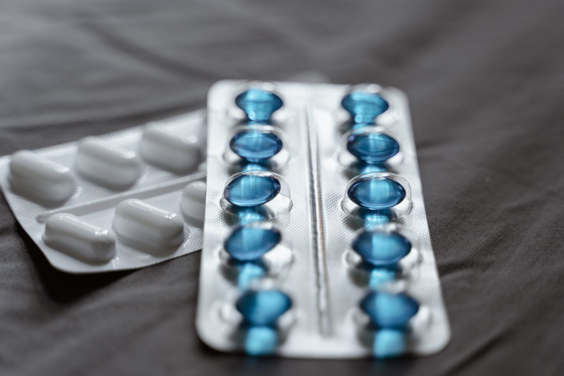 Vue détaillée des médicaments conditionnés sous blister, montrant les capsules molles bleues et les comprimés blancs.