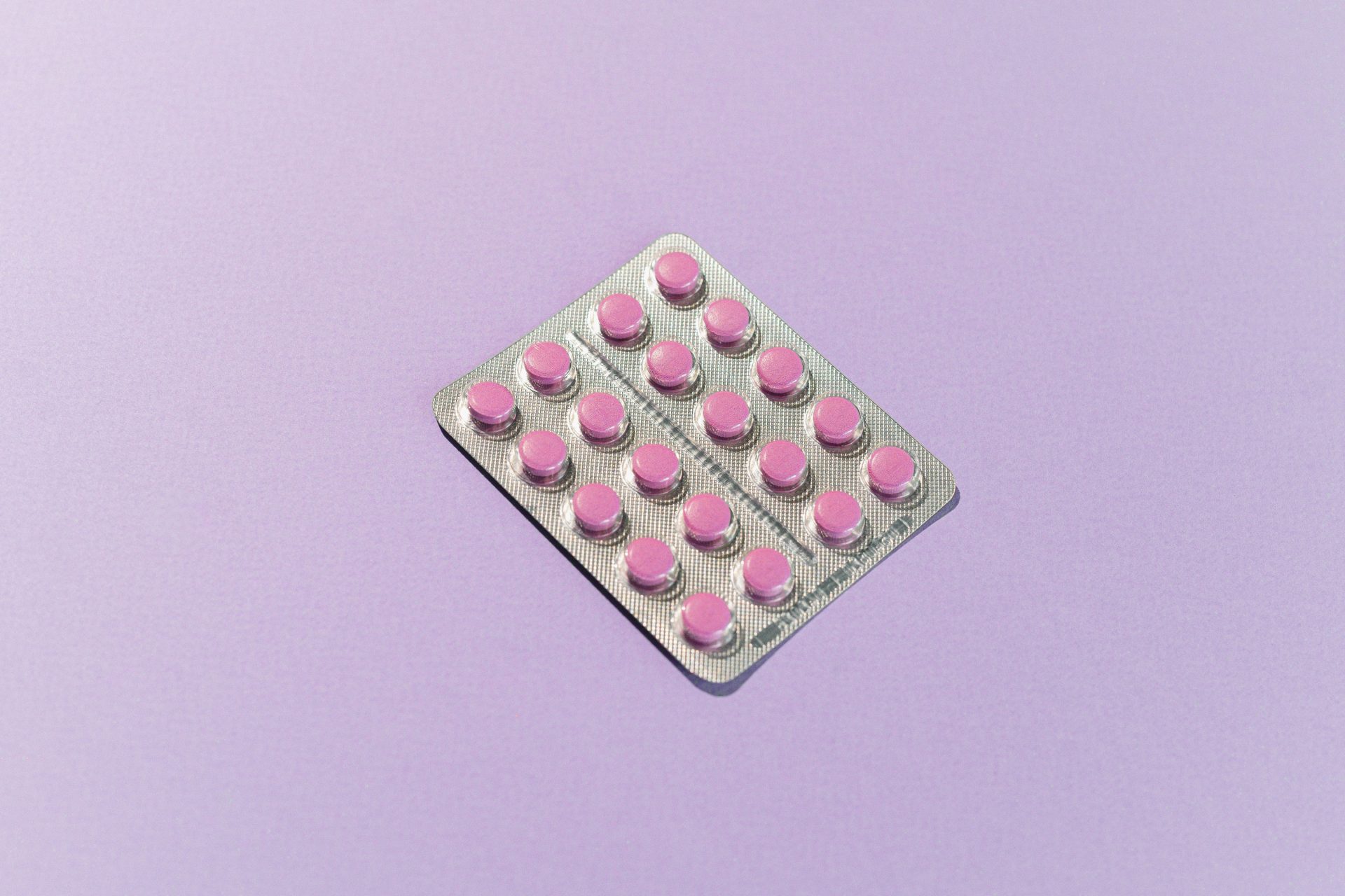 Plaquette thermoformée contenant des comprimés roses sur fond lavande, mettant en avant le thème de la santé.